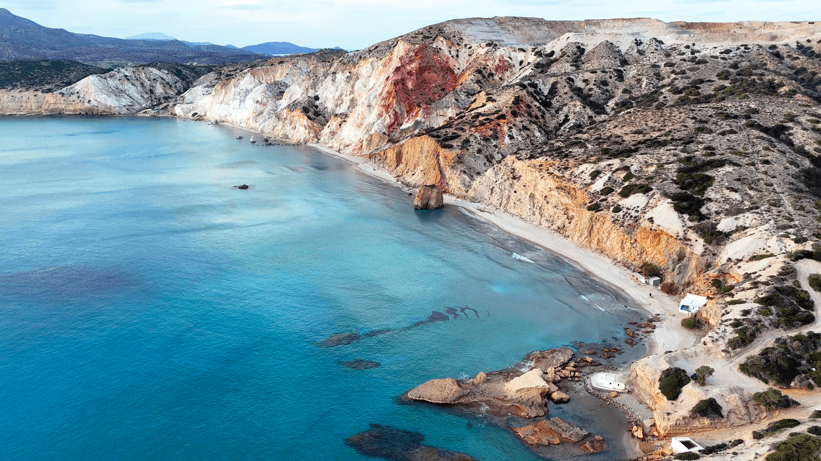 Turquoise shallow water and coloured cliffs at a beach on Milos