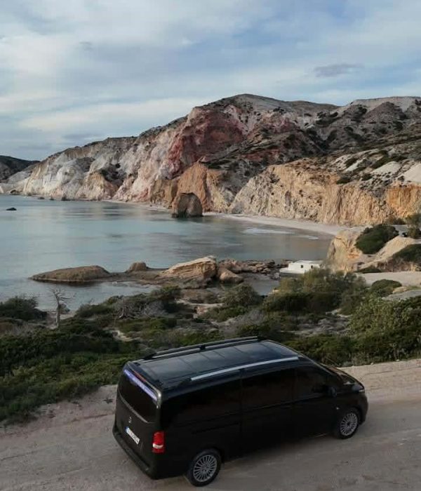 Elysium Transfer Milos minivan parked on a coastal road above a beach